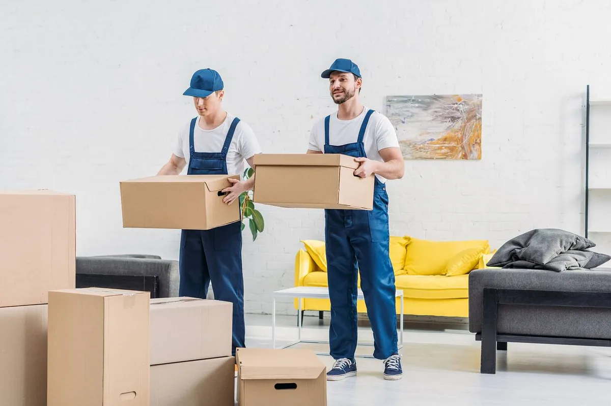Professional movers in uniform carrying boxes through home
